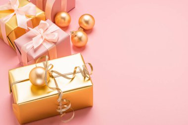 Saten kurdeleli şenlik kutuları. Altın oyuncak topları. Pastel pembe arka plan. Düz plan. Tatil konsepti. Boşluğu kopyala.
