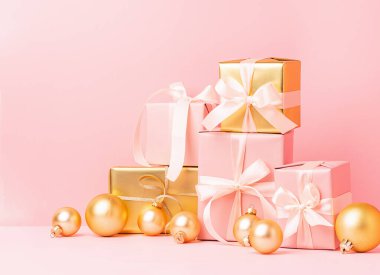 Pastel pembe arka planda saten kurdeleli oyuncak topları olan altın renkli kutular. Tatil konsepti. Ön görünüm