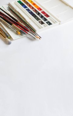 Boya fırçaları, beyaz arka planda yarı yalıtımlı çok renkli suluboya boyalar. Yer tasarımı metni olan düz düzen.