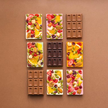 Çeşitli renklerde çikolatalar ve kahverengi arka planda meyveli fındık dilimleri olan renkli dolgular. Üst görünüm düz düzlem.