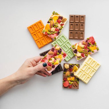 Parlak manikürlü kadın elinde çeşitli renklerde çikolatalar ve dilimlenmiş meyveli fındıklar tutuyor.