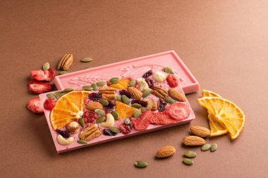 Kahverengi arka planda meyveli fındıklı çikolata pembesi. Tatlı yemek konsepti. Yatay çerçeve kopyalama alanı