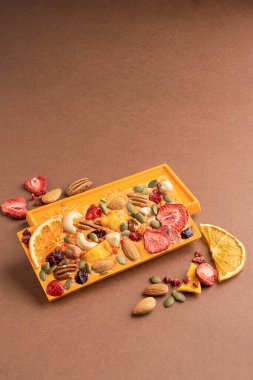 Kahverengi arka planda meyveli fındıklı çikolatalı turuncu fayans. Tatlı yemek konsepti. Dikey çerçeve kopyalama alanı