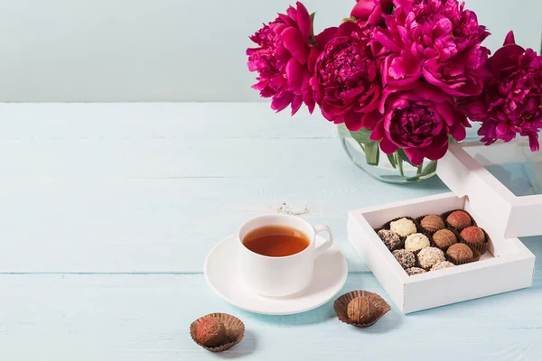 Bir fincan çay, burgundy çikolatası mavi, yumuşak arka planda güzel şakayıklar. Seçici odak kopyalama alanı. Üst görünüm