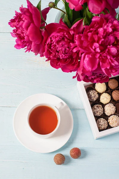 Copa de caja de té de chocolates borgoña hermosas peonías sobre fondo azul suave. Espacio de copia de enfoque selectivo. Vista superior — Foto de Stock