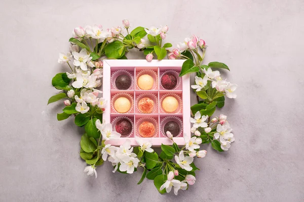 Çeşitli renkte çikolatalar, zarif bir kutunun içinde. Gri arka planda taze çiçeklerin süslendiği bir kutuda..