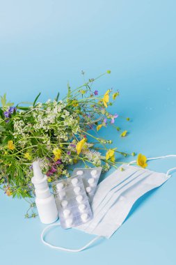 Mevsimsel alerjileri önleme kavramı. Taze çiçekler tıbbi maske hapları mavi arka plan düşürür..