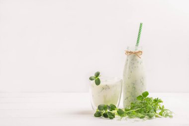 Süt ürünleri içeceği ve taze mikro çimenler beyaz mutfak masasındaki cam bardakta yeşillikler..