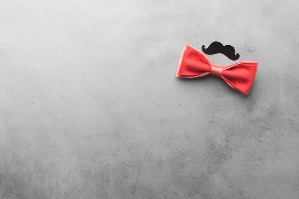 Decorative black mustache and red bow-tie on a gray background. The concept of mens holiday fathers day. Top view — Stock Photo, Image