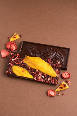Kahverengi arka planda çilekli mango dilimleri olan çikolatalı Belçika çikolatası. Tatlı yemek.