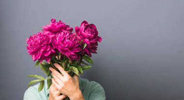 Güzel elbiseli bir kadın elinde gri arka planda büyük bir buket kırmızı şakayık tutuyor. Yatay çerçeve seçici odak kopyalama uzayı