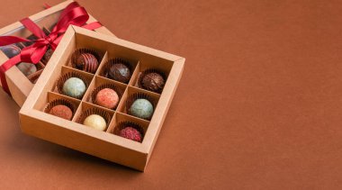 Saten kurdeleli koyu kahverengi arka planı olan bir kutunun içindeki çeşitli çikolata soslarından çikolatalı tatlılar. Bayramlık tatlı konsepti. Yatay çerçeve kopyalama uzayı. Üst görünüm düz düzlem