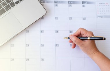 Yakın ve kadın el üst görünümü masada dizüstü bilgisayar ile takvim veya yıl planlayıcısı bir şey yazmak