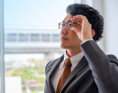 Yakışıklı ve akıllı asyalı adam yakından görünümü onun gözlük dokunun ve parlak geleceğe bakmak ve başarılı bir görünüm ile pencereye bakmak