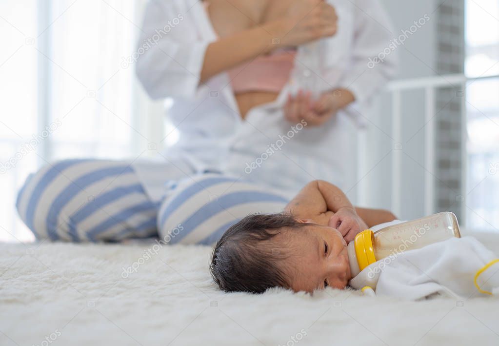 White shirt mother use breast milk pump to get breast milk and sitting near the sleeping newborn on white bed