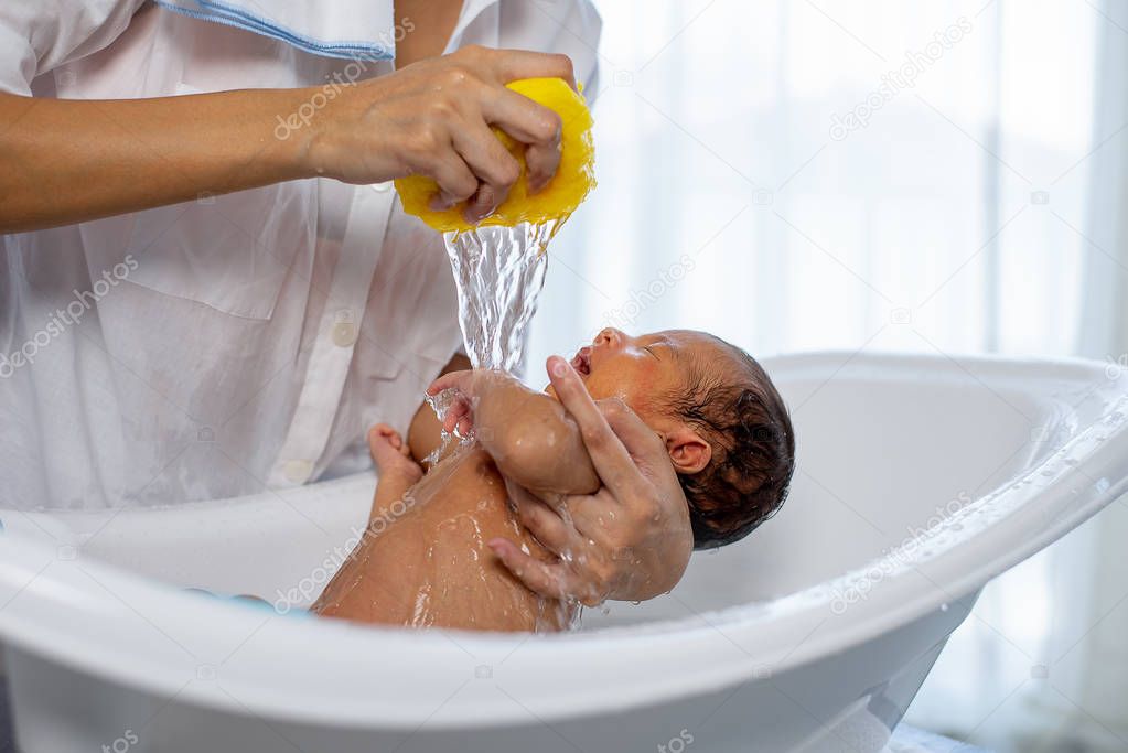 White shirt mother use yellow sponge to bath little newborn baby in white bathtub