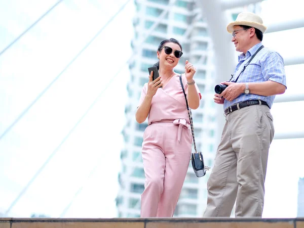 Couple of Asian old man and woman tourist are dancing among the big building of big city. This photo also contain concept of good life of elderly people.