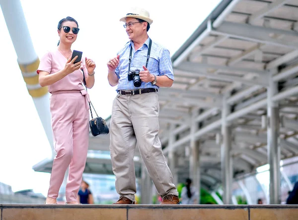 Couple of Asian old man and woman tourist are dancing among the big building of big city. This photo also contain concept of good life of elderly people.