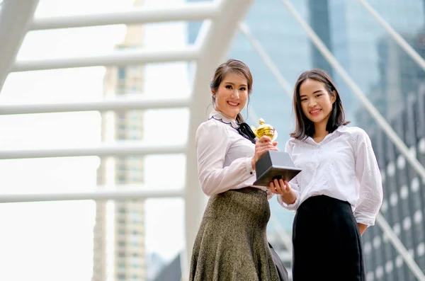 Beautiful business girls show their trophy of the success in her works and stand among the high building in the city.