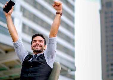 Beyaz iş adamı gün içinde şehir arasında sandalyeye oturarak elleri ile mutlu ve başarılı eylem göstermek.