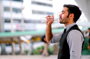 Beyaz iş yakışıklı adam serinlik için şehirde gündüz saatlerinde şişeden su içmek.