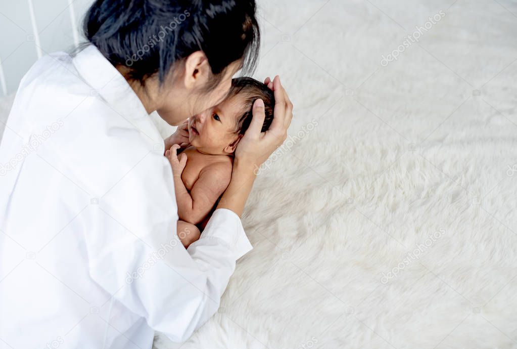 White shirt Asian mother is kissing and holding newborn baby near fluffy bed with concept love and careful for baby