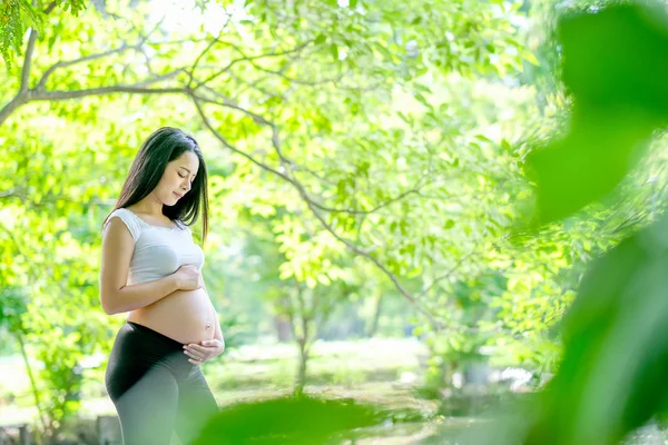 Piękne Azjatyckie Kobiety Ciąży Patrzeć Dotknąć Jej Brzuch Zielonym Tłem — Zdjęcie stockowe