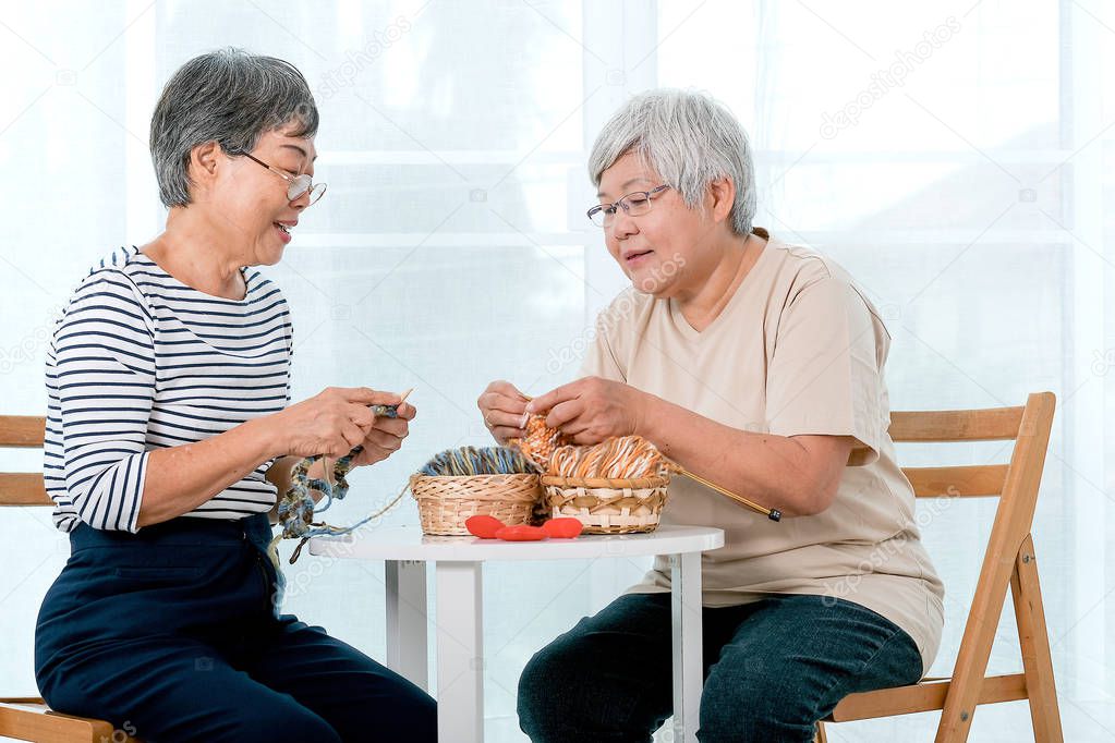 Two Asian elderly woman sit on chair and have activity of knitting, also talk together with smile in front of balcony.