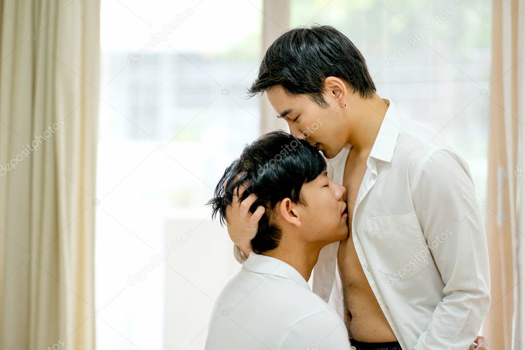 Asian gay couple hug together with one kiss to the other chest and one kiss head in the bed room with day light.