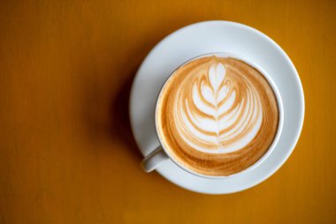 Düşük ışık ile kahverengi ahşap masada latte sanat ile kapuçino beyaz bir fincan.