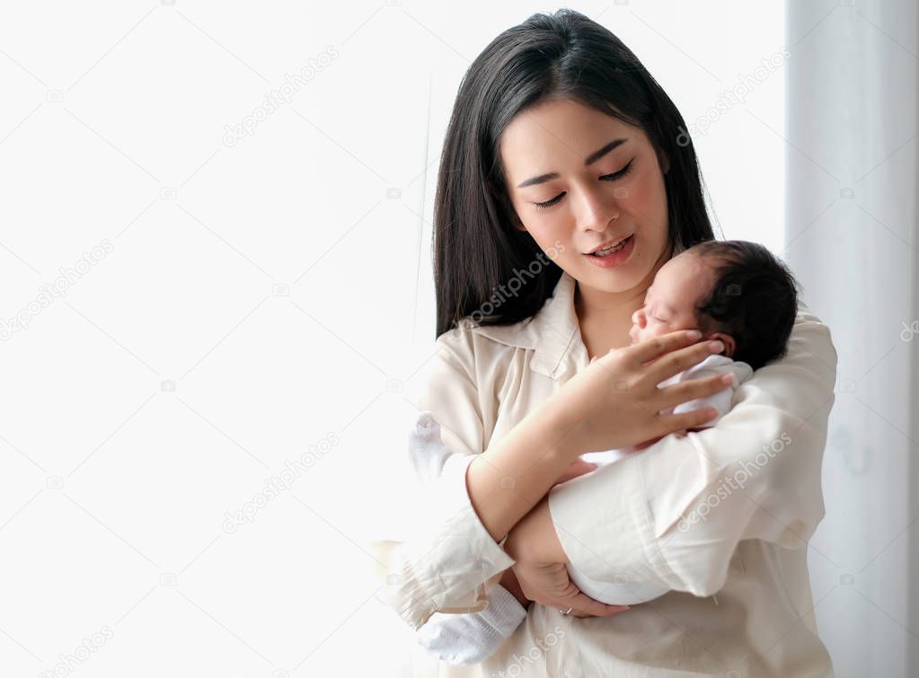 Beautiful Asian mother talk to her newborn baby in front of white curtain with day light.
