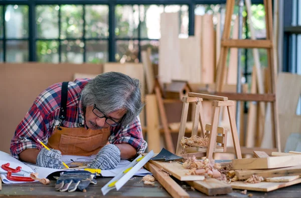 Old Asian craftsman act as write something on the paper in the room with wood pile and surround with glasses.