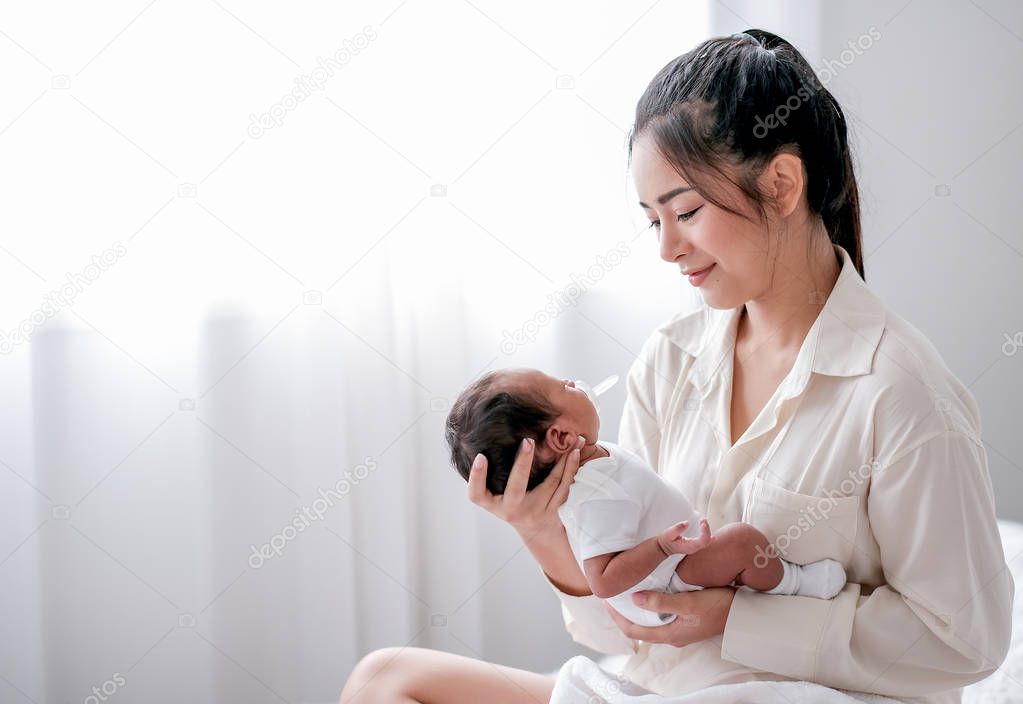 Asian mother hold or carry her newborn baby and look to baby face with love in bedroom.