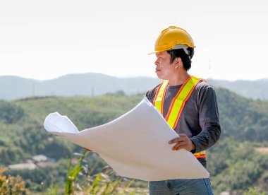 İşçi ya da toprak taşıma operatörü inşaat kâğıdı planını tut ve dağ manzarasının önüne bak..
