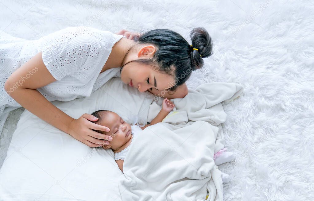 Top view of Asian mother lie and sleep with her newborn baby on white bed.