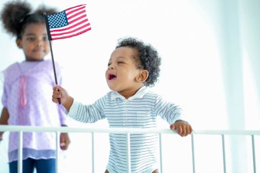 Küçük Afrikalı Amerikalı çocuk, elinde Amerika Birleşik Devletleri bayrağını tutuyor ve gülümsüyor genç bir kızla oynaşmanın keyfini çıkarıyor gibi görünüyor. Evde iyi yaşam koşulları kavramı.