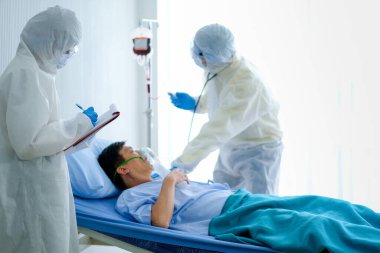 Covid Klinik Koruma Odası 'ndaki tüm vücut koruyucu kıyafetleriyle sağlık görevlileri hastaya yatakta destek ve tedavi sağlıyorlar. İyi sağlık bakım sistemi kavramı, hastanın terapisini destekler.