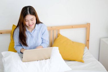 Güzel bir kadın çalışmak için dizüstü bilgisayar kullanır ve yatak odasında mutlu görünür. İş hayatında daha iyi sonuç elde etmek için evde çalışmanın mutluluk kavramı.