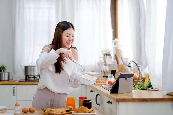 Beautiful woman show action of cooking to the tablet look like she present to friends. Concept of online communication help and support of easy way to work from home.