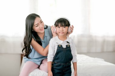 Anne kulaklığı tut ve kızına sabah ışıklarıyla yatak odasında müzik dinlettir. Aile içinde iyi ilişki kavramı ve evdeki yeni normal yaşam tarzı.