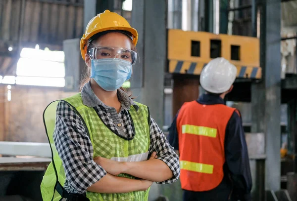 Factory woman engineer worker or technician with hygienic mask stand with confident action with her co-worker in workplace. Concept of good industrial system for better manufacture business