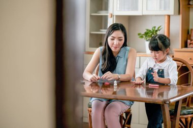 Asyalı anne ve kız gün ışığında mutfakta birlikte kil modelleme oynuyorlar ve mutlu görünüyorlar. Evlerinde farklı yaşlarda olan aile zamanlarının tadını çıkarma kavramı.