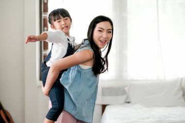 Asyalı küçük kız, gün ışığıyla annesine oyun oynarken eğleniyor. Evlerinde farklı yaşlarda olan aile zamanlarının tadını çıkarma kavramı.