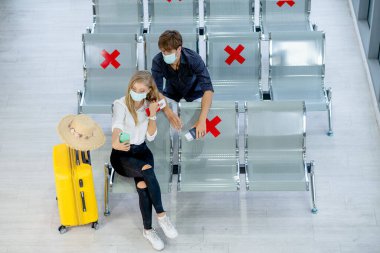 Kafkasyalı sevgililerin üst düzey görüntüsü maskeli kadın ve erkek sosyal mesafeli sandalyede oturuyorlar ve Covid-19 salgınından kurtulduktan sonra seyahat sırasında havalimanında selfie çekiyorlar..