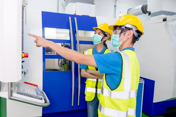 Beautiful factory worker woman with mask discuss the working details of machine with co-worker in factory workplace. Concept of good management system in industrial business support employee working.