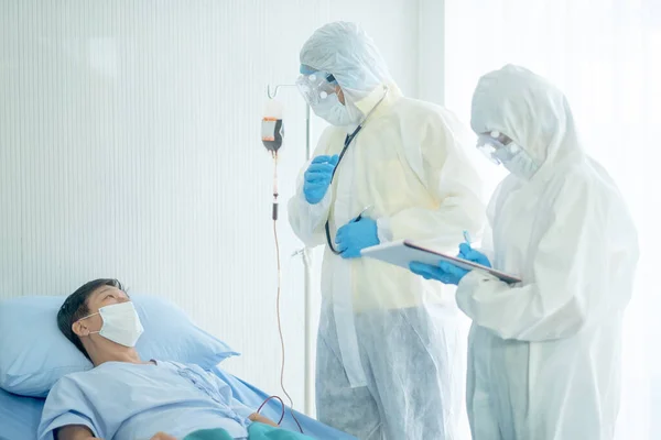 Doctor with whole body cover suit explain about patient disease progression and nurse record the data beside Covid-19 patient bed.