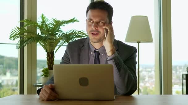 白人のビジネスマンは 携帯電話で話し オフィスでラップトップコンピュータを使用しています — ストック動画
