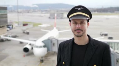 Genç erkek pilot, karlı havada havaalanında poz veriyor.