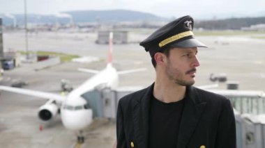 Genç erkek pilot, karlı havada havaalanında poz veriyor.