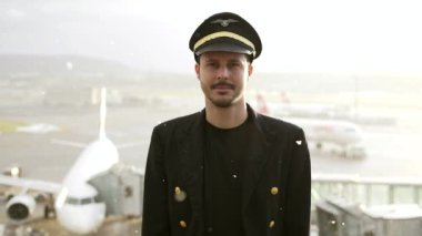 Genç erkek pilot, karlı havada havaalanında poz veriyor.